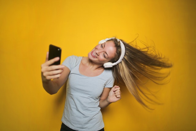 Tančící dívka s mobilem v ruce a sluchátky na uších